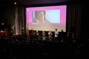 Das Team des Kurzfilms "Tischrebellen" vor der Leinwand. Der Film basiert auf dem Drehbuch "Tischmanieren", mit dem Autor*innen Linn und Luka Peltzer 2019 den Publikumspreis gewannen.