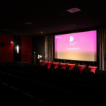 Noch leerer Saal 1 im Kieler Studio Filmtheater mit Sitzplätzen für die Lesenden und Logo vom Drehbuchpreis Schleswig-Holstein im Hintergrund.