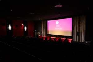 Noch leerer Saal 1 im Kieler Studio Filmtheater mit Sitzplätzen für die Lesenden und Logo vom Drehbuchpreis Schleswig-Holstein im Hintergrund.